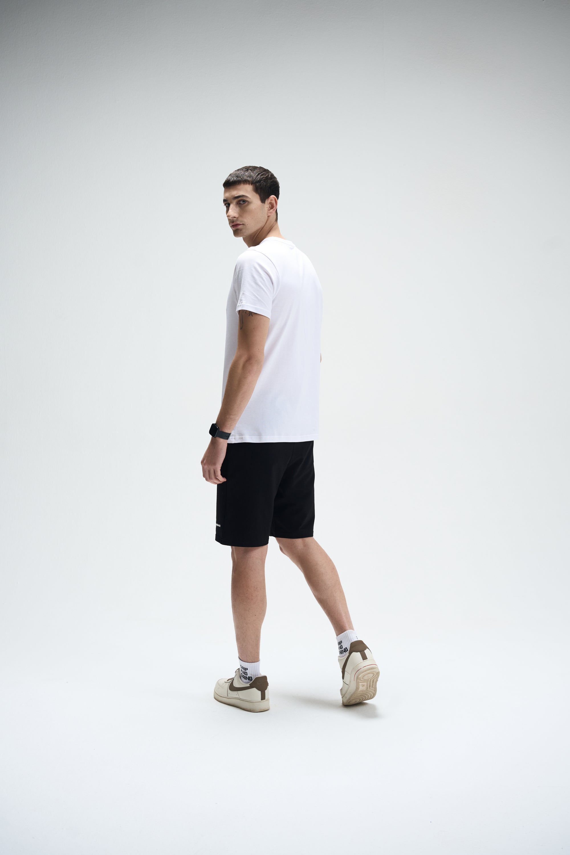 Men's white SoftLuxe crew neck T-shirt with black shorts and beige sneakers, back view.