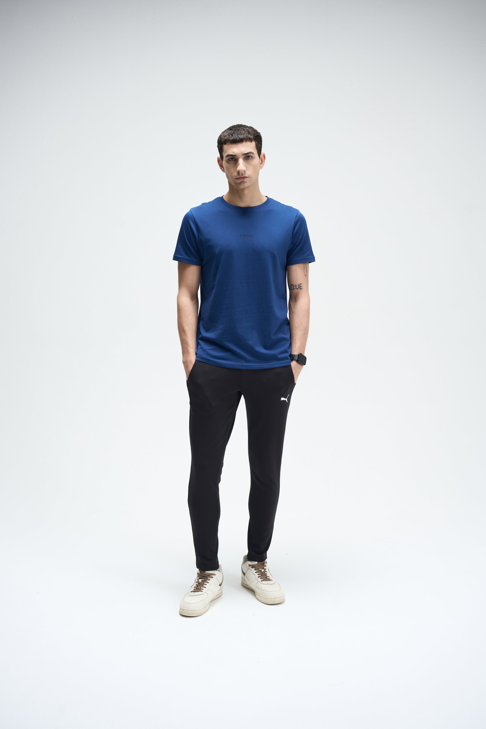Men's navy blue SoftLuxe Crew T-shirt with short sleeves, paired with black joggers and beige sneakers.