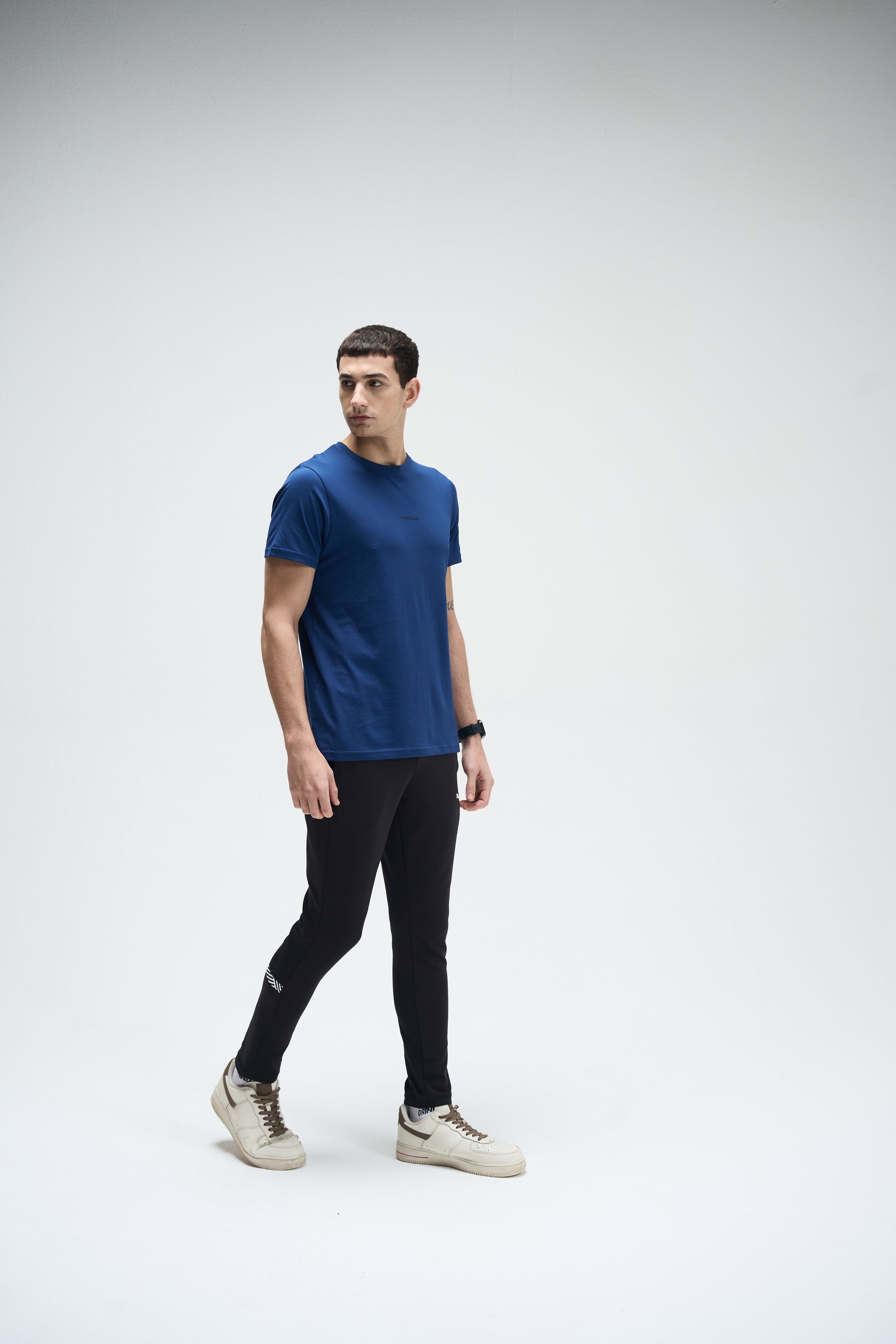 Men's navy blue SoftLuxe Crew T-shirt paired with black slim-fit jogger pants and beige sneakers.