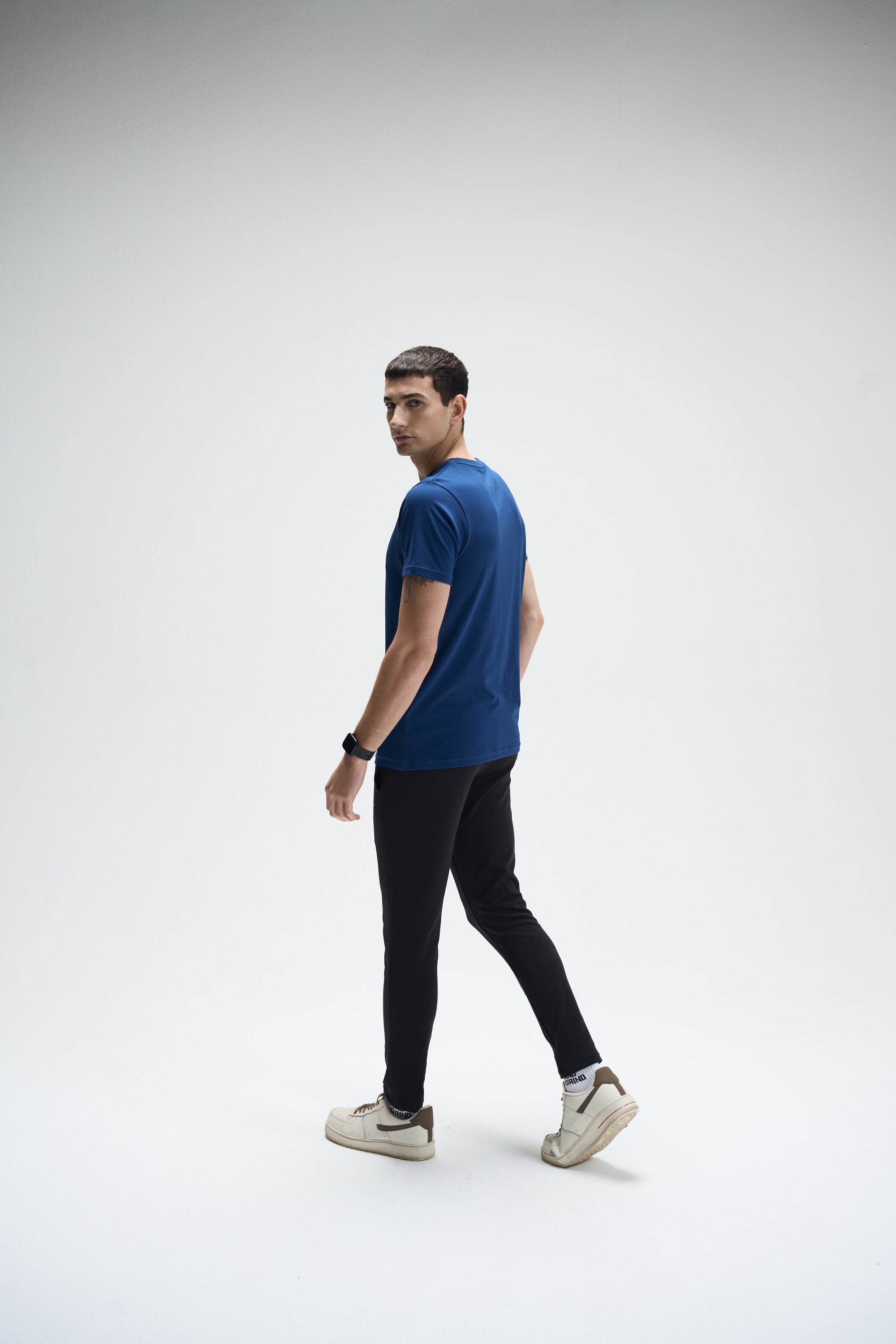 Men's navy SoftLuxe Crew T-shirt with regular fit, paired with black pants and beige sneakers.