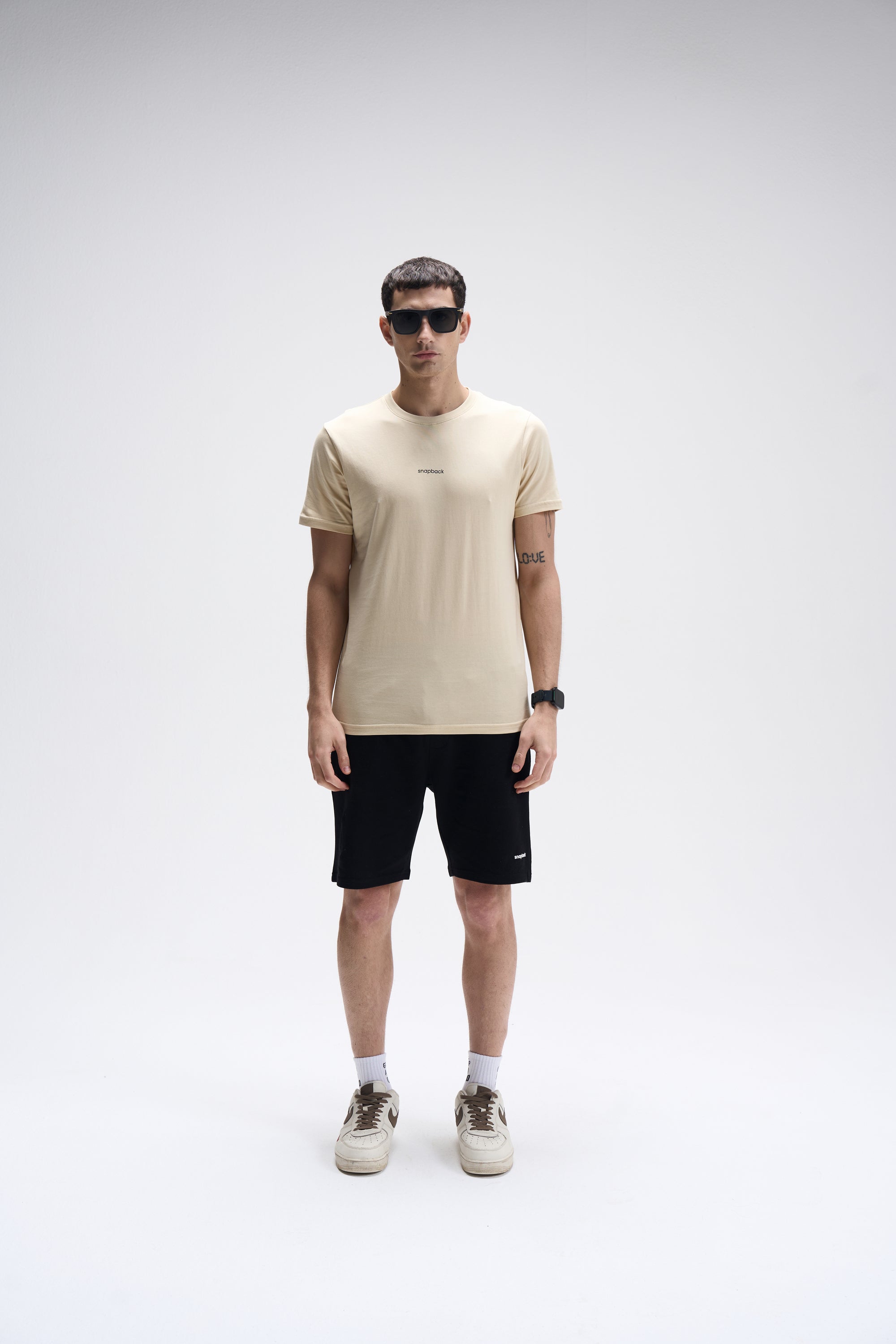 Men's regular fit crew neck T-shirt in soft summer sand color paired with black shorts and white sneakers.